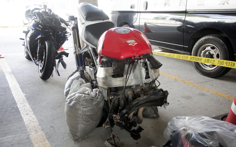A motorcycle missing its front tire and propped up by sandbags sits in front of another motorcycle in a garage.