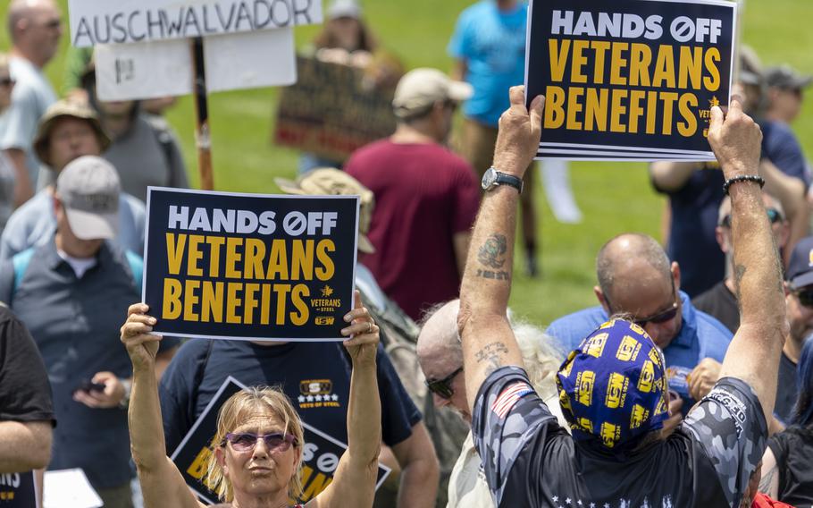 Two protesters hold signs reading “Hands off veterans benefits.”