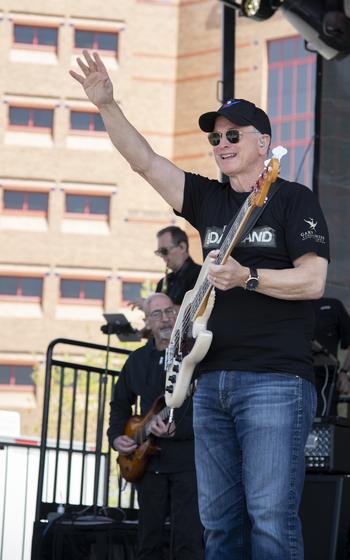 Gary sinise with a guitar and an arm in the air on stage