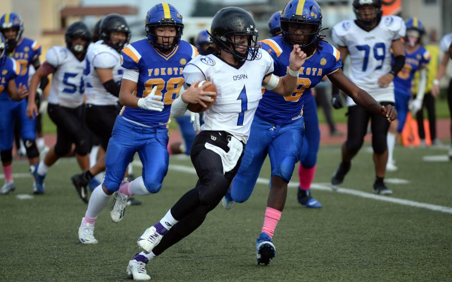 Osan quarterback Joshua Low tries to outrun Yokota defenders Theo Shone and Jamani Fields.