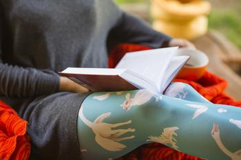 Nestled in a cozy corner, a reader loses themselves in a vibrant story, wrapped in a warm throw and adorned with whimsical patterned leggings that bring a splash of color to the serene setting.
