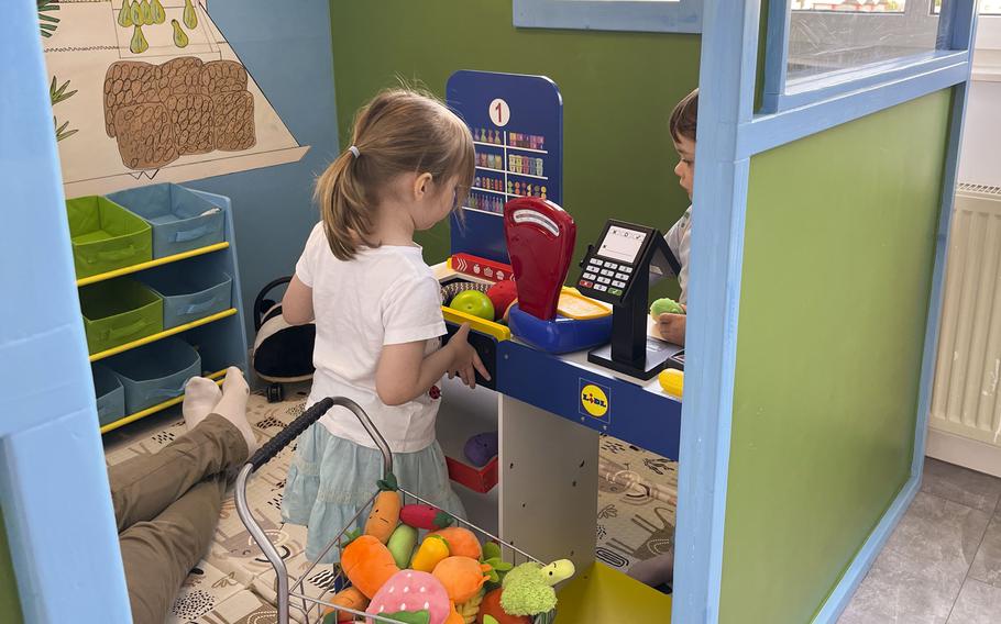 Small children interact at the cash register of a pretend grocery store. 
