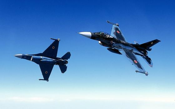 Two military jets fly next to each other in formation.