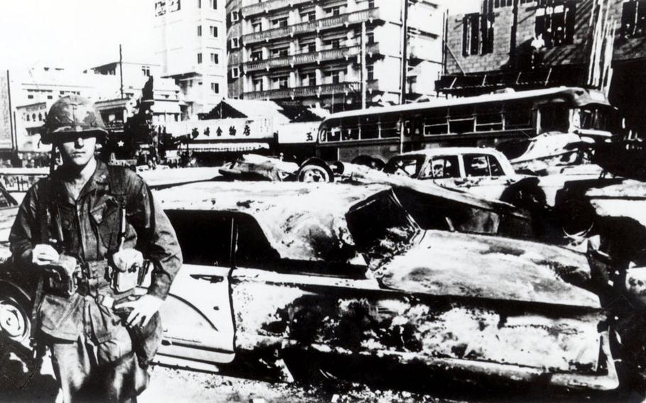 A American service member stands in front of a burned car in Koza, now known as Okinawa city, after the Koza Riot of Dec 20, 1970.