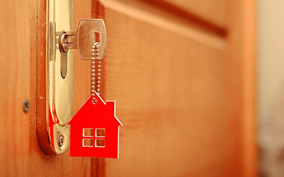Key with house shaped keychain in door, closeup. 