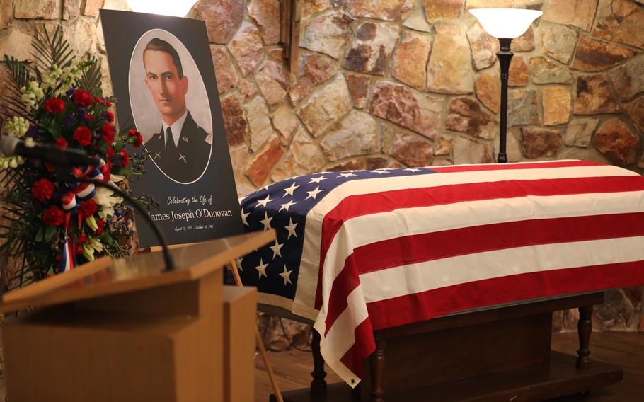 A portrait of O’Donovan on a table, with flowers, next to a flag-draped casket.