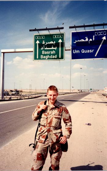 A soldier stands on the side of a road in the desert.