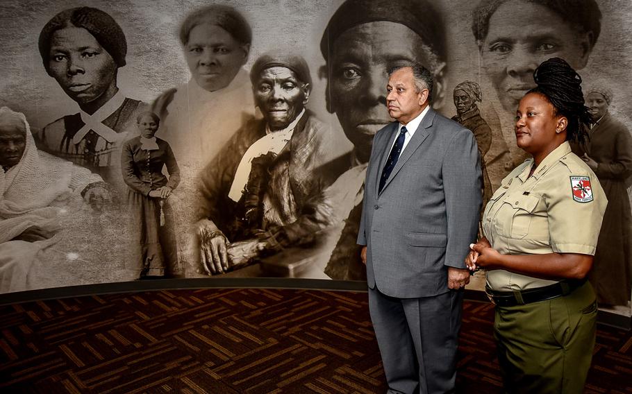 A man and woman stand in an exhibit adorned by historic photos.