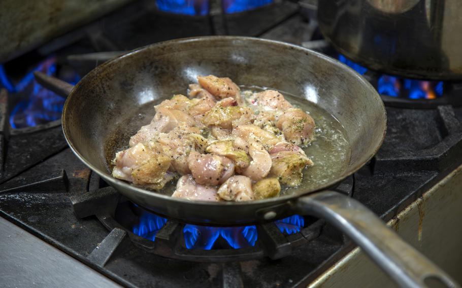 A close-up view of meat cooking in a metal pan on a stovetop burner.