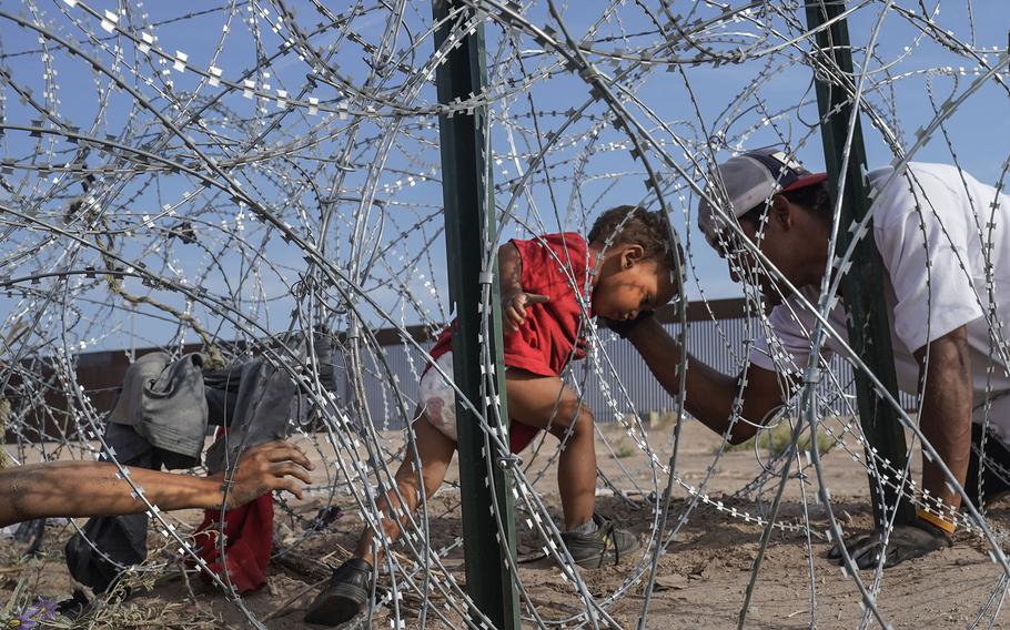 Venezuelan migrants guide a child through the razor wire near the U.S.-Mexico border in Ciudad Juárez on Thursday, Sept. 21, 2023.