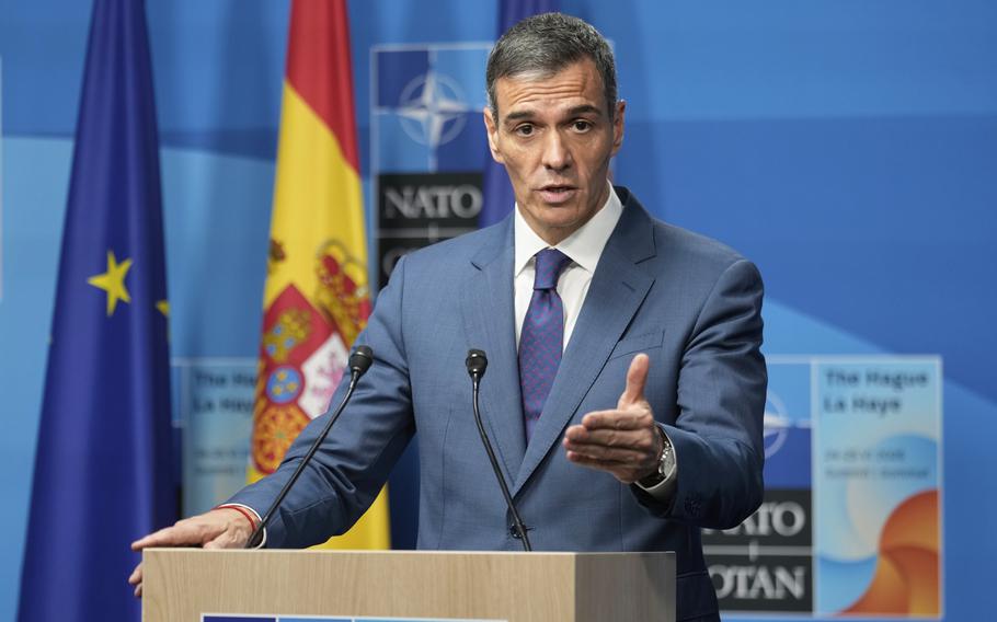 Spain’s prime minister speaks at a podium while gesturing with one hand.