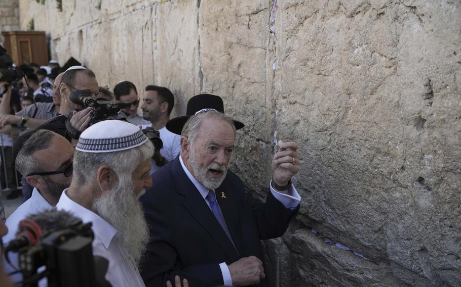 Mike Huckabee holds a small note in his hand while surrounded by photographers and people at the Western Wall in Jerusalem.