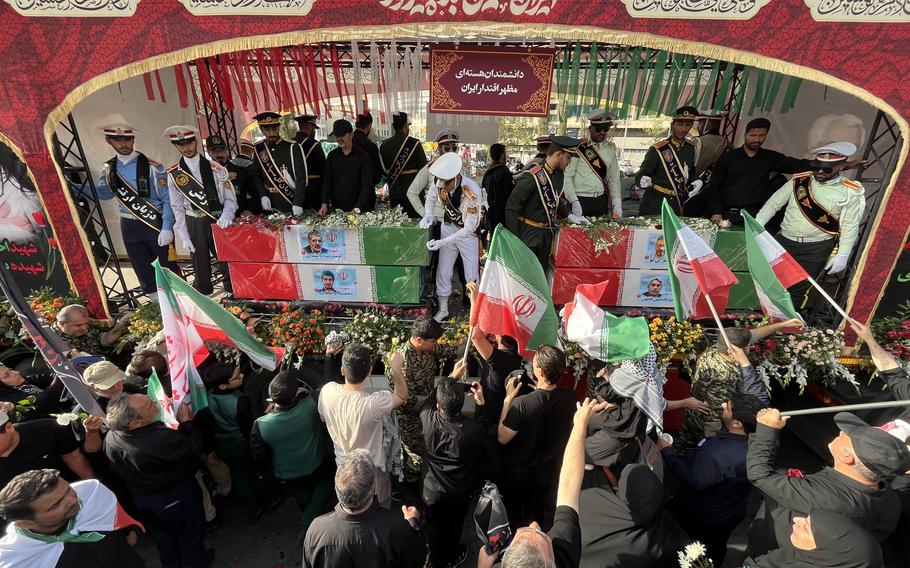 Dozens of people stand around two coffins draped in the Iranian flag 