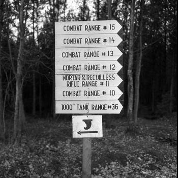 A signpost in a forested area indicates directions to various base ranges.