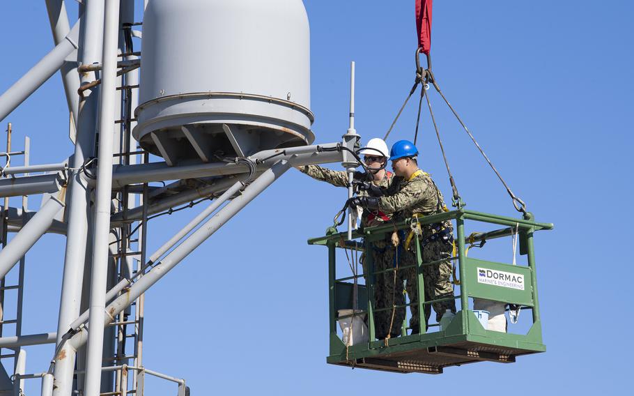 Petty Officers 2nd Class Nathan A. Milca, right, and Drake W. Childers perform maintenance on the forward house antennae aboard the expeditionary sea base USS Hershel “Woody” Williams while moored in Cape Town, South Africa, for maintenance, Oct. 5, 2021. 