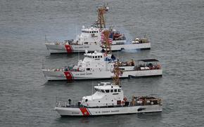 Three Coast Guard ships idle next to each other in open water.