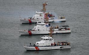Three Coast Guard ships idle next to each other in open water.