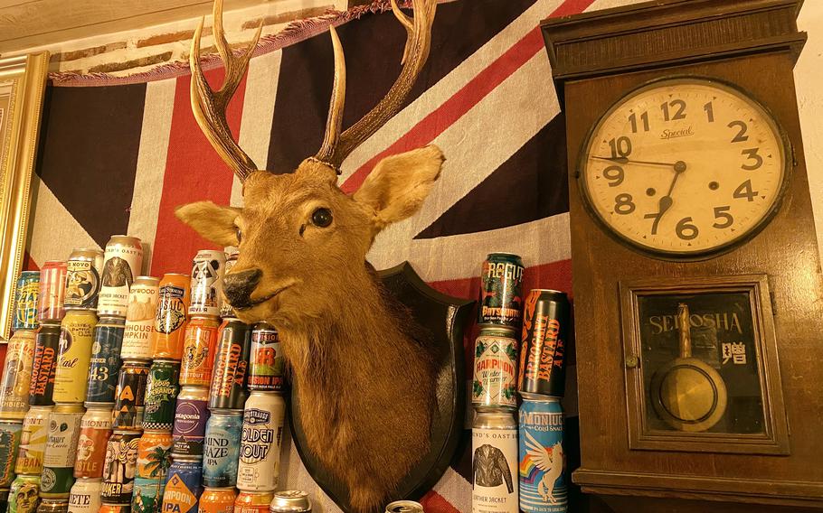 A wall displays an antlered deer head, a clock, stacks of eclectic beer cans and a Union Jack flag.