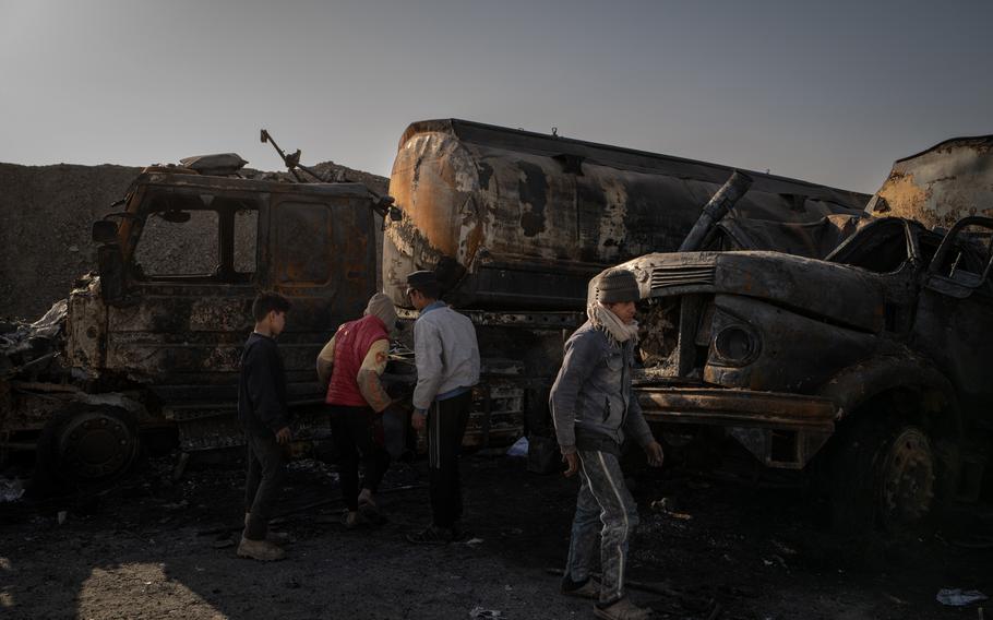 Boys inspect burned-out oil tankers for scrap metal across the road from the prison complex in Hasakah, Syria. The trucks were set ablaze in the attack. 