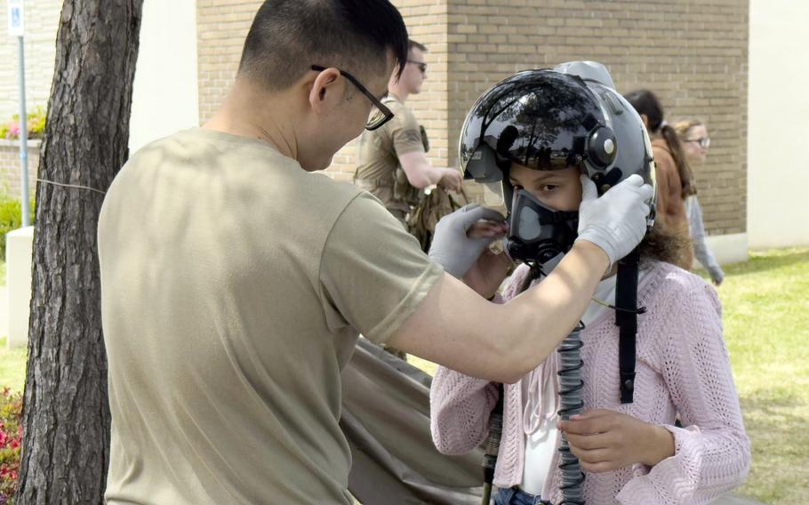 An airman adjusts the fit of an oxygen mask on a girl wearing a fighter pilot helmet. 