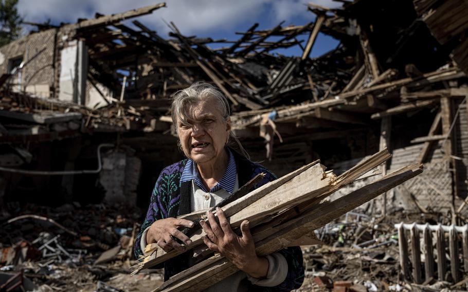 A woman collects wood for heating from a destroyed school where Russian forces were based in the recently retaken area of Izium, Ukraine, Monday, Sept. 19, 2022. 