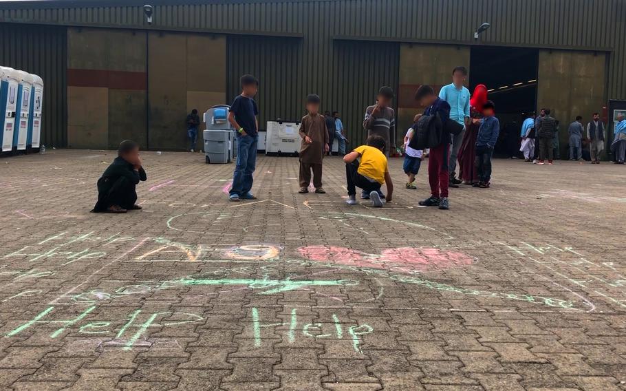 Afghan boys draw the word "help" and a broken heart with chalk on paving slabs at Rhine Ordnance Barracks in Kaiserslautern, Germany, Aug. 30, 2021. The children's faces have been blurred to protect anyone they may have left behind in Afghanistan.