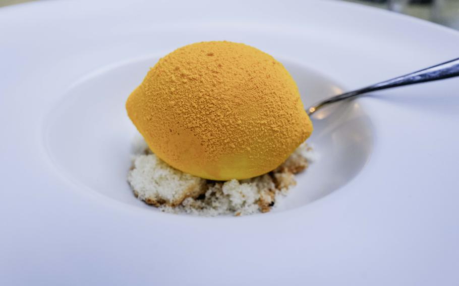 A visually deceptive white chocolate dessert shaped and colored like a lemon, featuring a tangy citrus center, is reminiscent of the popular "Is it cake?" memes, at Grifo Restaurant in Kerzenheim, Germany.