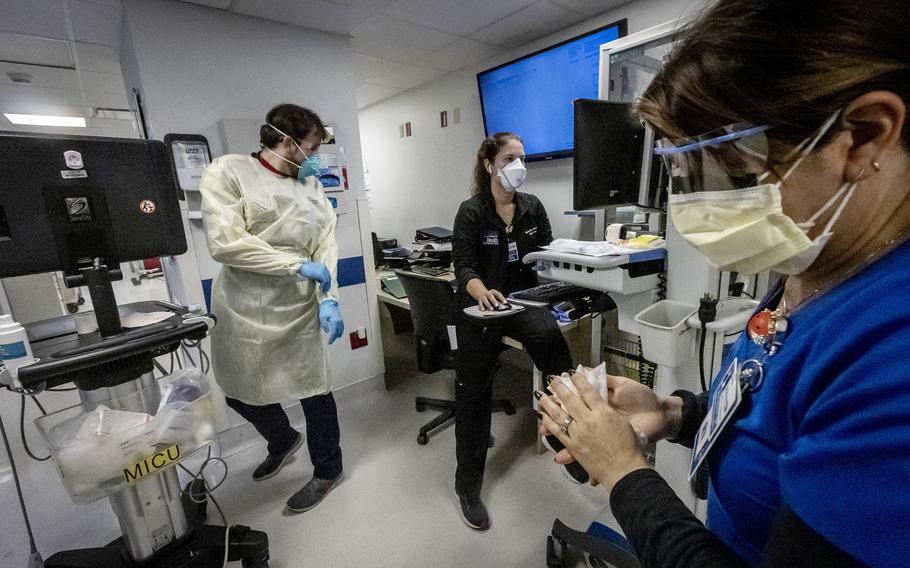 Nurse Alix Zacharski, right, sanitizes her hands as other doctors and nurses continue to care for a patient in the Medical Intensive Care Unit for COVID-19 patients at Jackson Memorial Hospital on July 23, 2021. 