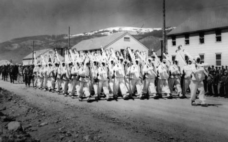 10th Mountain Division soldiers parade down a street at Camp Hale, Colo., probably in 1943. They are wearing their “whites” — winter camouflage uniforms — and carry white skis on their right shoulder as rifles are normally carried while on parade.