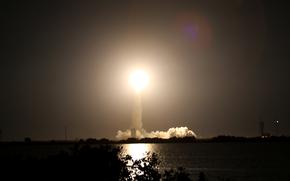 A bright light in the middle of a dark sky caps off a large plume of smoke.