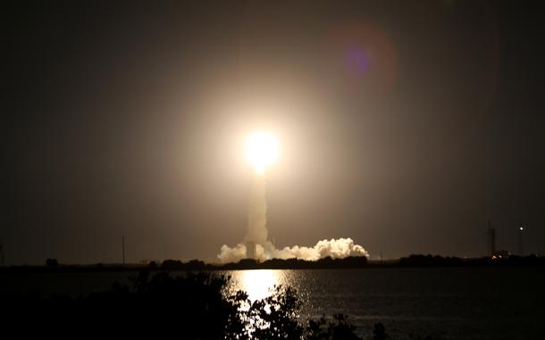 A bright light in the middle of a dark sky caps off a large plume of smoke.