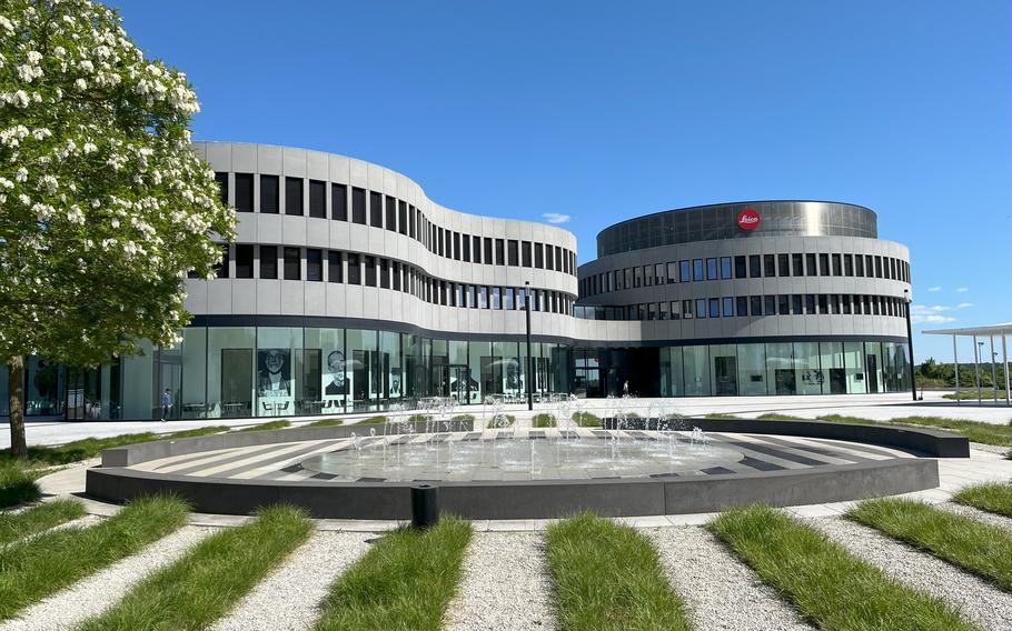 A modern building with a curved glass facade has a fountain in front of it.