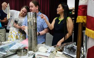 Three adults look at items in plastic bags that were put into a silver tube time capsule when they were children.