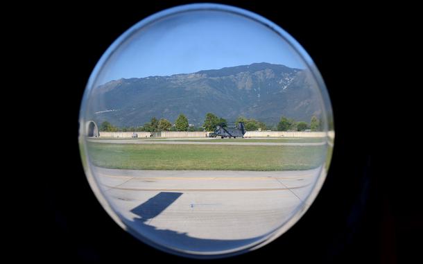 A mountain and military helicopter are seen through a circular window.