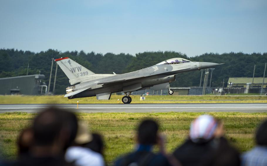 A military F-16 fighter jet lands on a runway at an airfield with spectators watching in the foreground. 