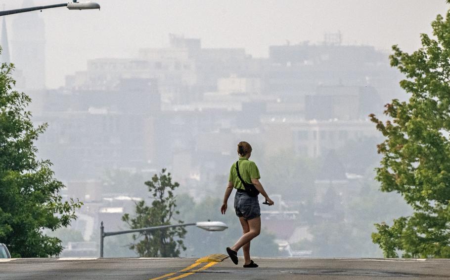 A woman crosses a street as smoke from the Canadian wildfires renders the cityscape amorphous in Washington, D.C.