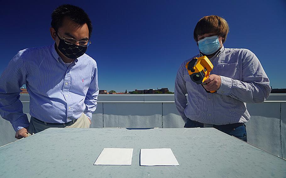 Purdue researchers Xiulin Ruan, left, and Joseph Peoples use an infrared camera to compare the cooling performance of white paint samples on a rooftop. 