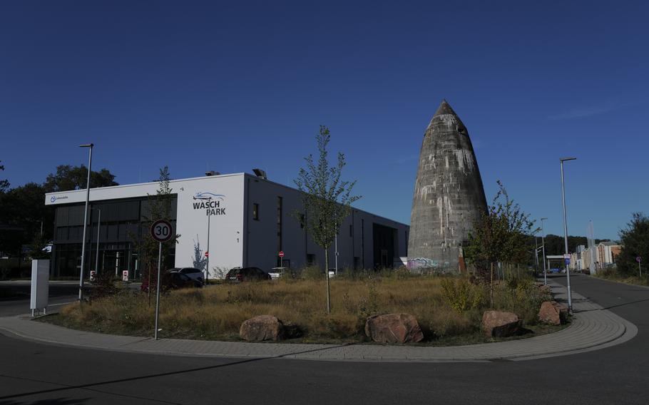 A Spitzbunker stands next to a modern car wash on Pariser Strasse in Kaiserslautern, a stark reminder of the city's wartime past amidst its contemporary landscape. The structure is under protection as a historical structure and modern construction projects had to adjust around its real estate.