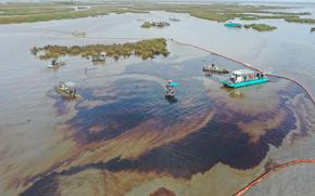 An aerial photo of an oil spill in a marsh environment, with a handful of boats in the water.