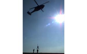 A vertical photo of a helicopter in the air lifting a figure at the bottom of the photo.