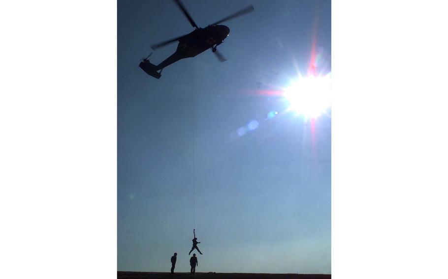A vertical photo of a helicopter in the air lifting a figure at the bottom of the photo.