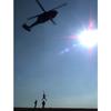 A vertical photo of a helicopter in the air lifting a figure at the bottom of the photo.