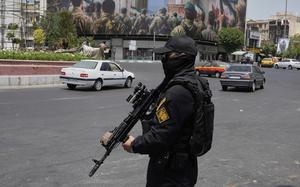 A man in a black uniform and mask carries a rifle.