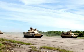 Multiple M1 Abrams tanks conduct training exercises. The tanks are positioned across a wide paved area with dust visible around them.