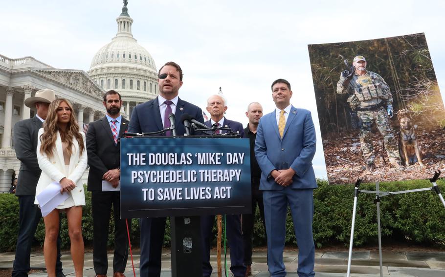 Rep. Dan Crenshaw, R-Texas, speaks at a Capitol Hill press conference on the Douglas “Mike” Day Psychedelic Therapy to Save Lives Act, Wednesday, June 14, 2023. On the right is a photo of Day, a Navy SEAL who suffered 27 gunshot wounds in Iraq and took his own life in March 2023.