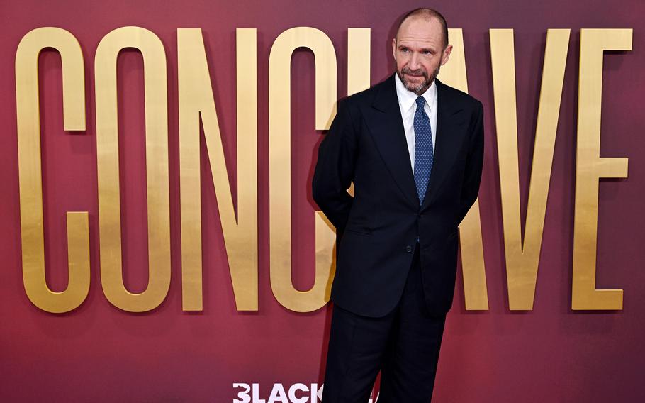 Ralf Fiennes in front of a sign for the film Conclave.
