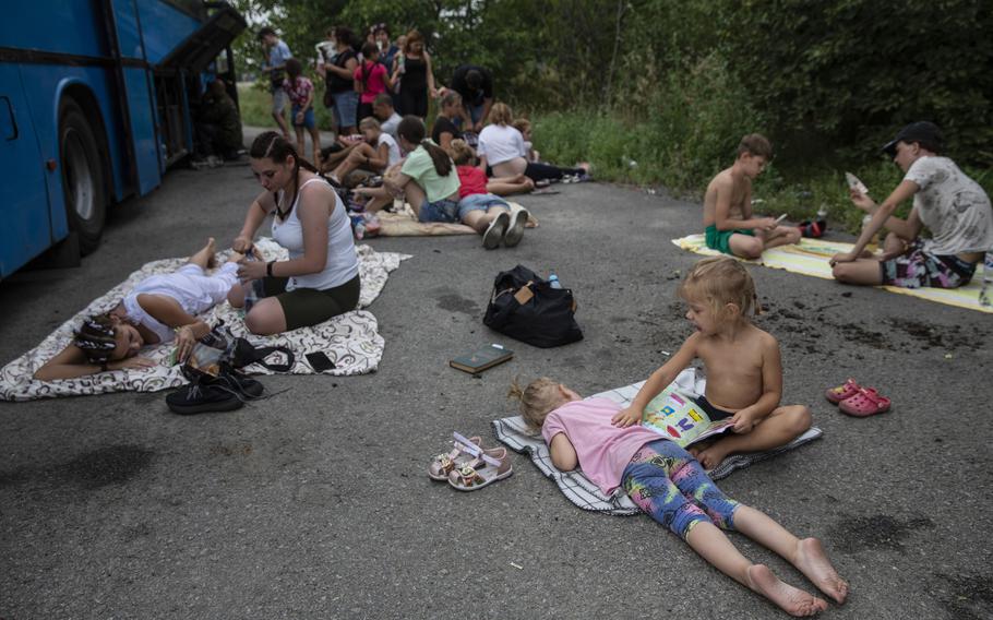 Ukrainian families that have fled areas under the control of Russian forces wait next to a broken-down bus near Chervonokamyane, Ukraine, on Aug. 15, 2022.