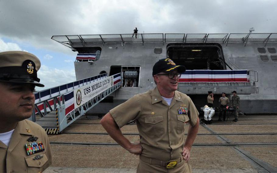 Command Senior Chief Raymond Cabral, left, and Cmdr. Christopher W. Wolff, commanding officer of LCS-26, speak on May 20 ahead of commissioning ceremonies for the Littoral Combat Ship named for the city of Mobile. Wolff sports the "plank holder" belt buckle limited to the vessel's crew at its commissioning. The buckles bear the ship's motto, "Victory Through Perseverance," and the purple-and-gold logo of a Mardi Gras flag used in Mobile.