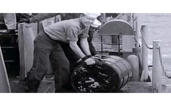 A video screen grab shows sailors aboard the USS Calhoun County (LST 519) rolling 55-gallon drums containing radioactive material into the sea in November 1957.