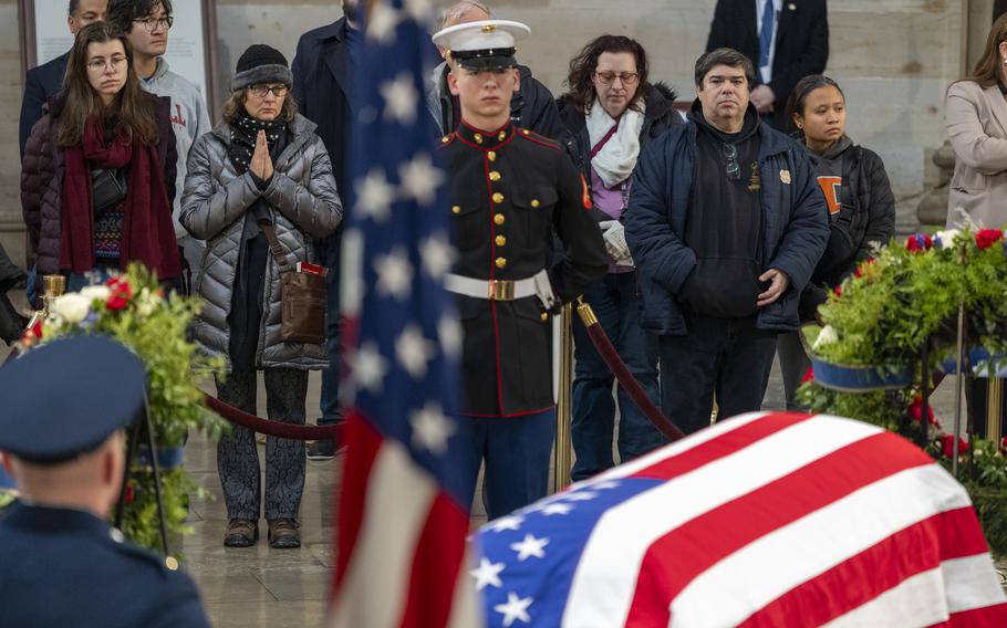 A Marine stands at attention near the flag-draped casket of Jimmy Carter as a crowd gathers at the Capitol.